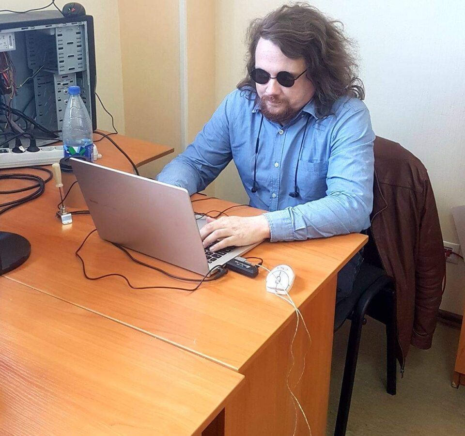 Илья Овсянников за столом, работает на ноутбуке