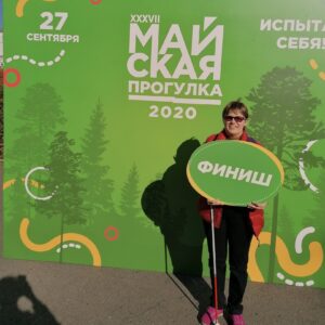 Улыбающаяся Маргарита Мельникова с табличкой "Финиш" на фоне щита с надписью "27 сентября, 37-я майская прогулка 2020»