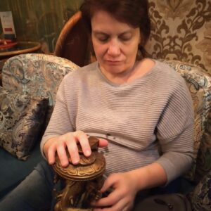 Наталья Демьяненко сидит в кресле и держит в руках деревянную фигурку. 
