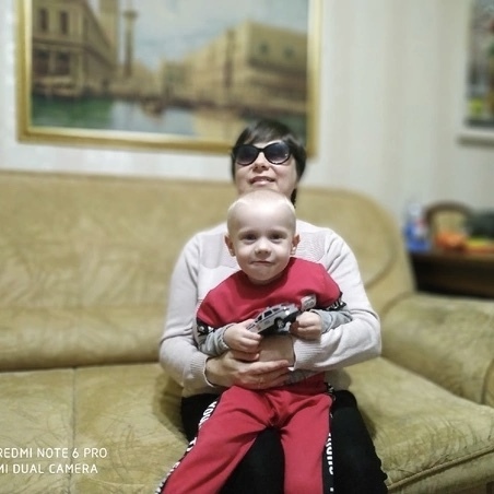 Улыбающаяся Александра Скоробогатова сидит на диване и держит на коленях сынишку, у того в руках игрушечная машинка