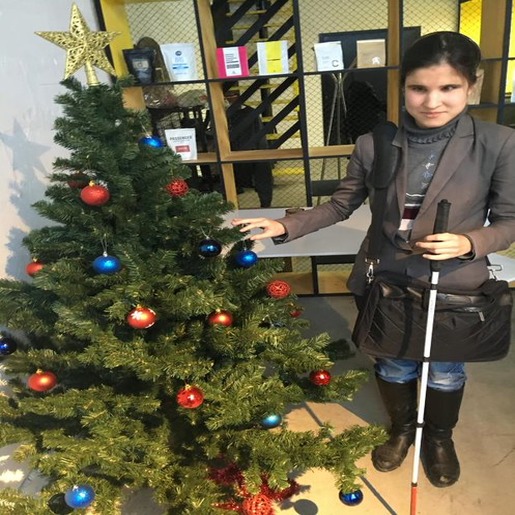 Алия Нуруллина с тростью в руке стоит возле новогодней елки, украшенной красными и синими шарами