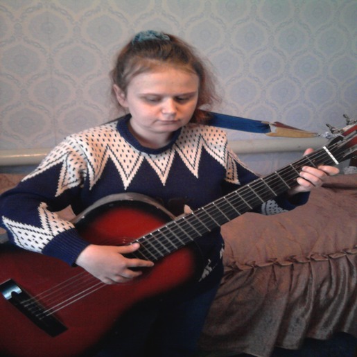 Виктория Аксенченко сидит на кровати и играет на гитаре