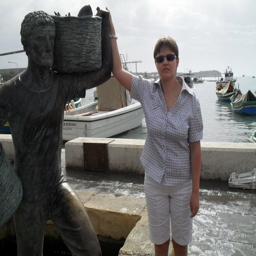 Маргарита Мельникова стоит, опираясь рукой на скульптуру в виде мужчины с корзинами в руках