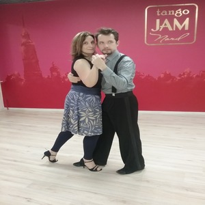 Наталья Катырина с партнером танцуют танго на фоне красной стены с надписью tango jam.