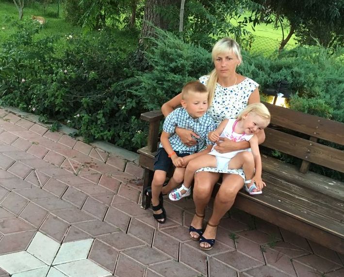 На фото в парке на скамейке сидит женщина с двумя детьми.