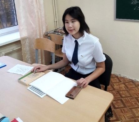 Марина Данилова сидит в классе за столом учителя