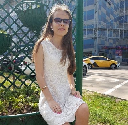 Кристина Павлова в светлом платье сидит на улице на фоне зелени
