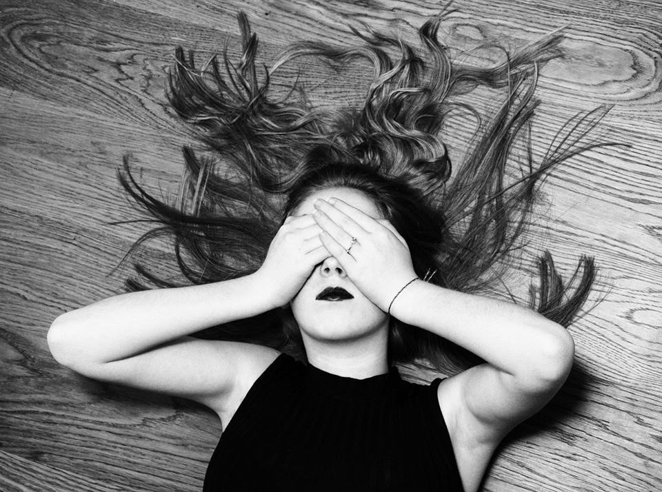 Изображение: девушка с длинными волосами лежит на полу лицом вверх, закрыв глаза руками