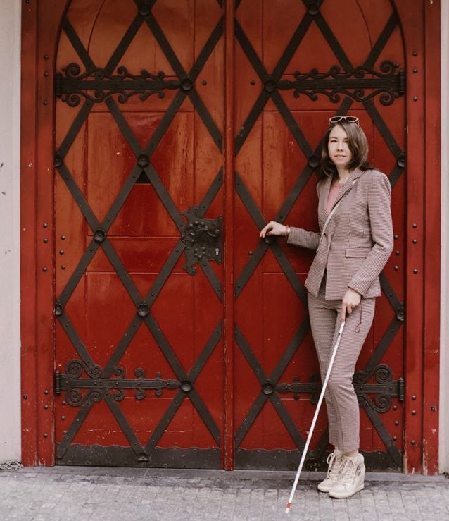 Ксения Энилина стоит с тростью на фоне старинных ворот