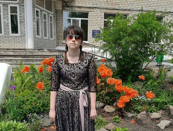 Елизавета Лошкарева стоит у школы на фоне клумбы с яркими цветами
