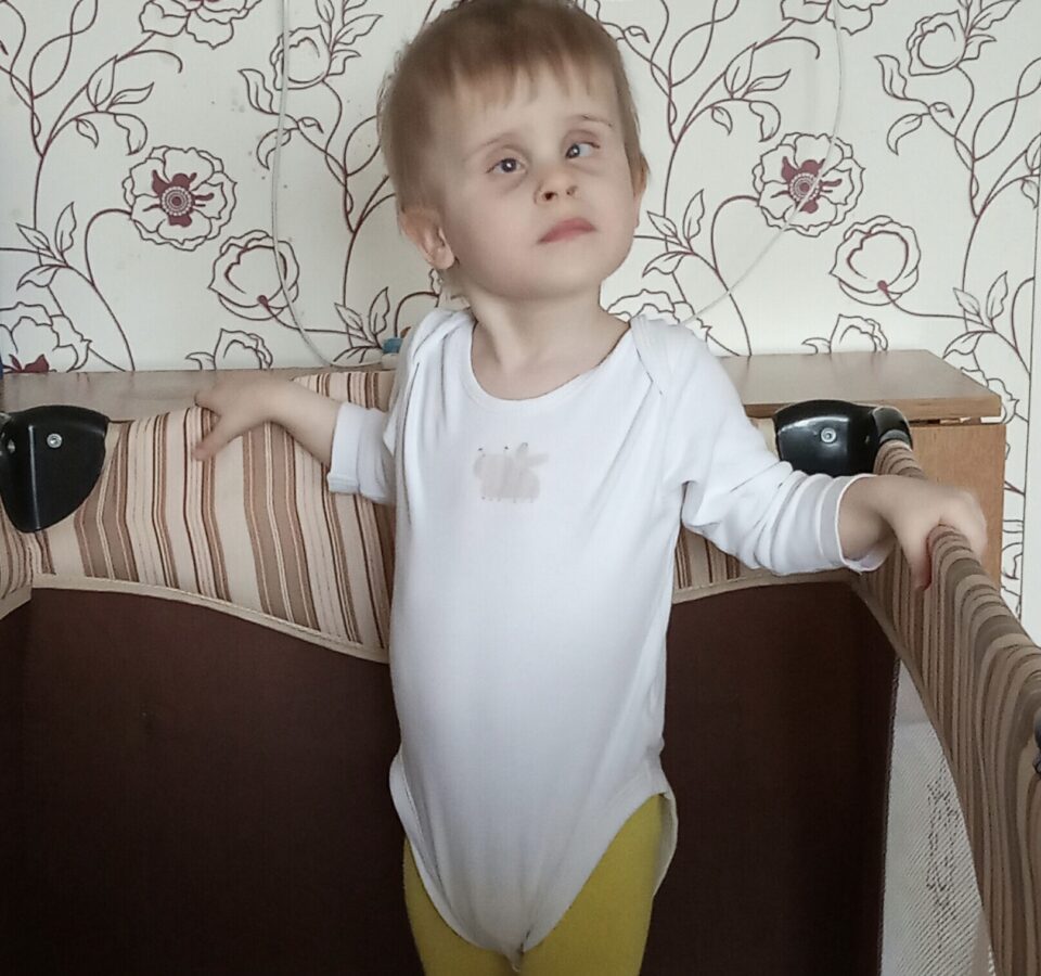 Малыш стоит в детской кроватке, опершись обеими руками о ее бортики