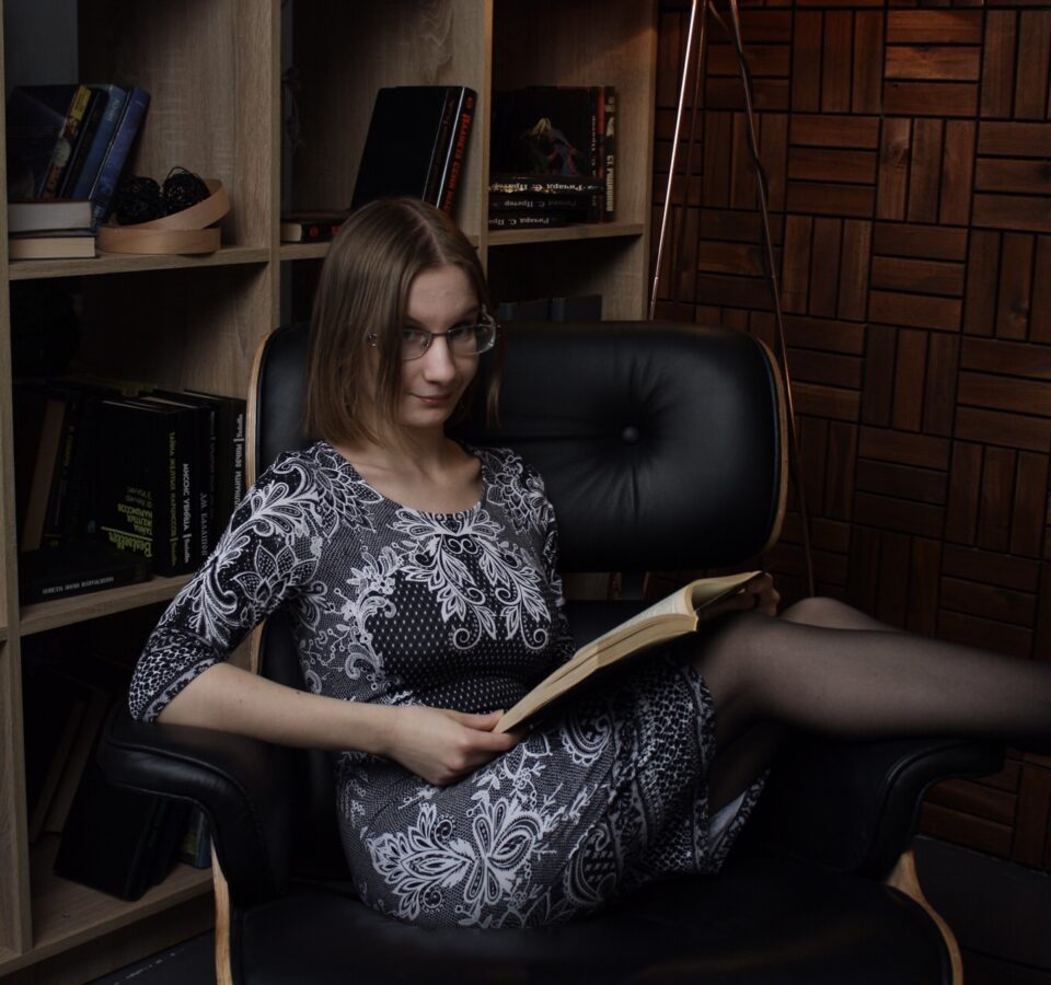 Мария Торгашева сидит в кресле с открытой книгой на коленях