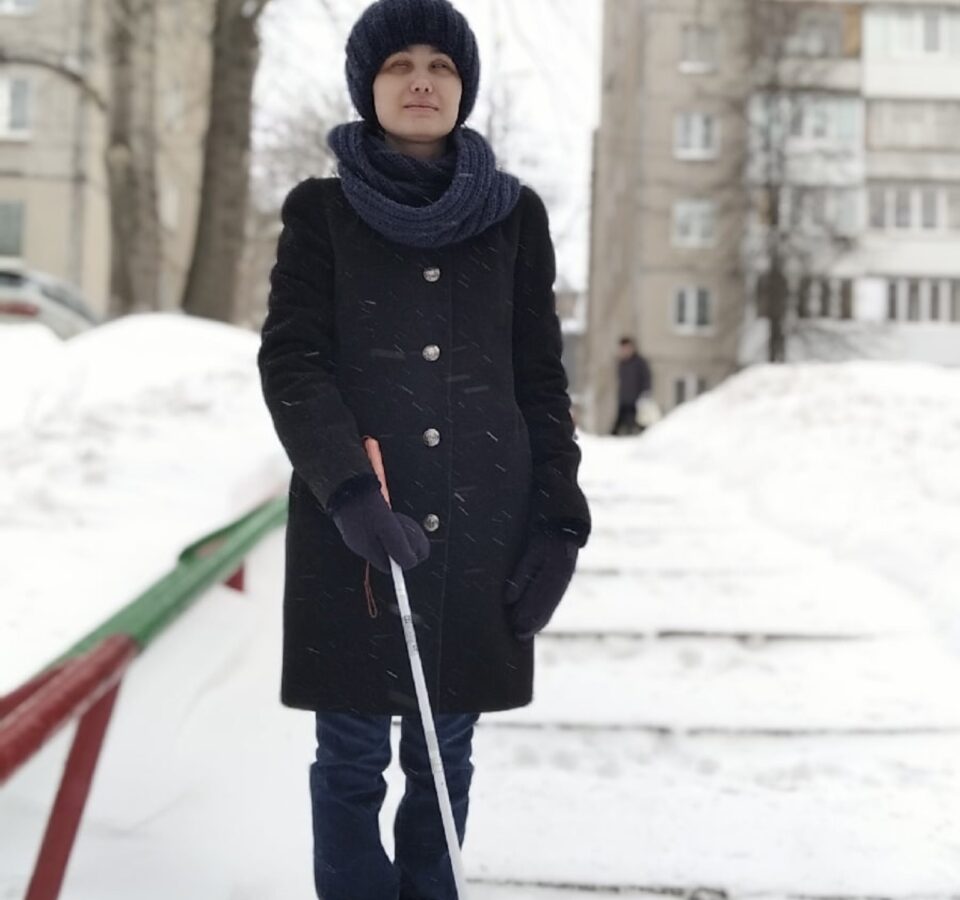 Надежда Долматова стоит с тростью в руках на заснеженной дорожке на фоне многоэтажных домов.