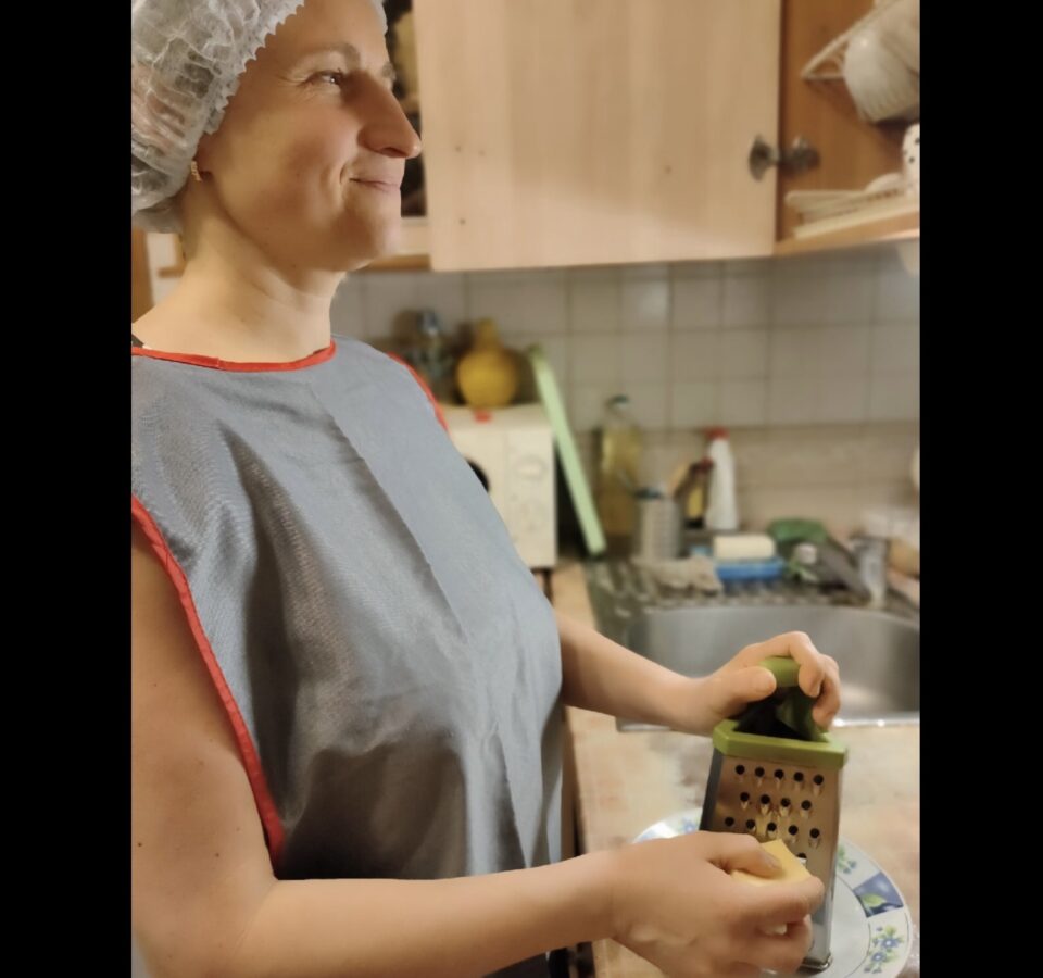 Мария Воеводкина в фартуке стоит на кухне, что-то трет на терке и улыбается