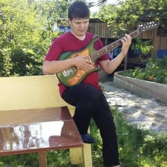 Георгий Бритько сидит на скамейке в саду и играет на электрогитаре