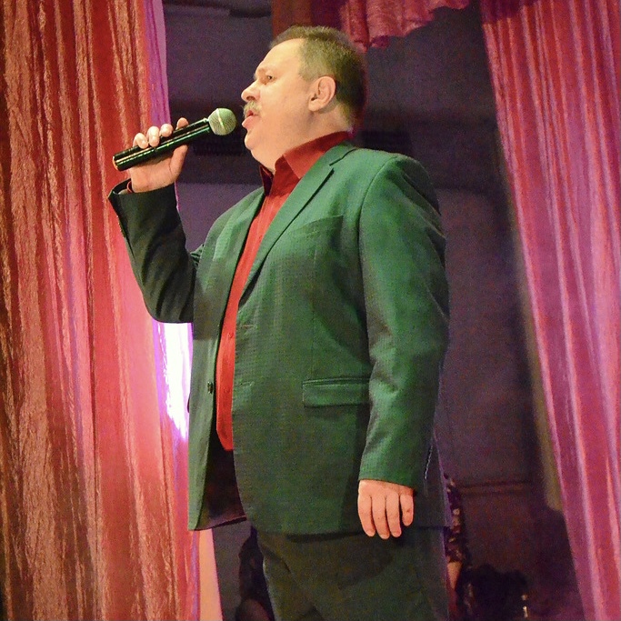 Андрей Калинин в зеленом костюме самозабвенно поёт на сцене в микрофон